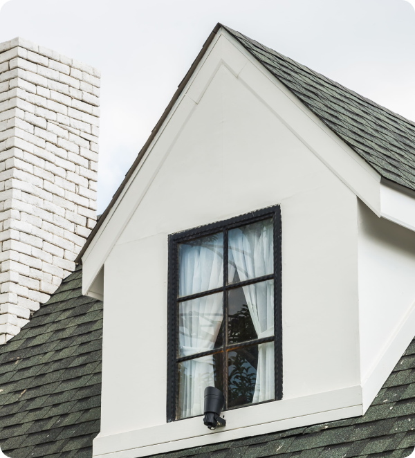 Close-up of a slanted roof with a chimney and window.