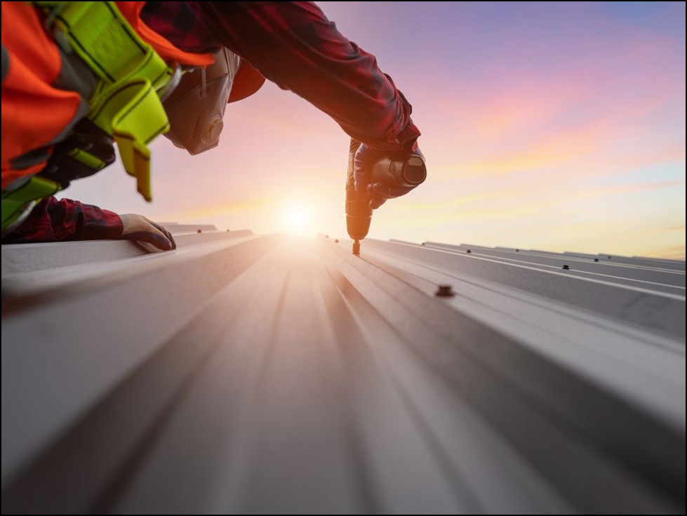 Roofer securing metal roof panel during sunset