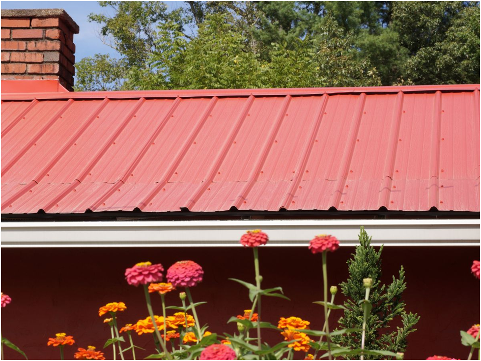 Red metal roof on home with flowers and chimney in view