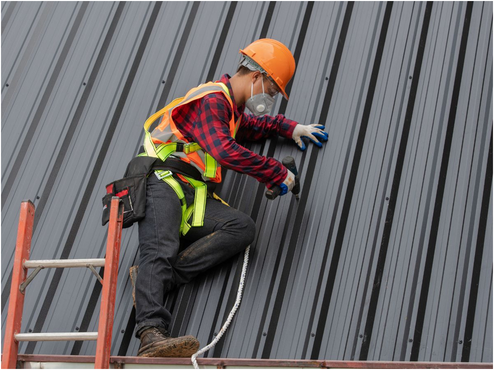 Roofer in safety gear installing black metal roof panels