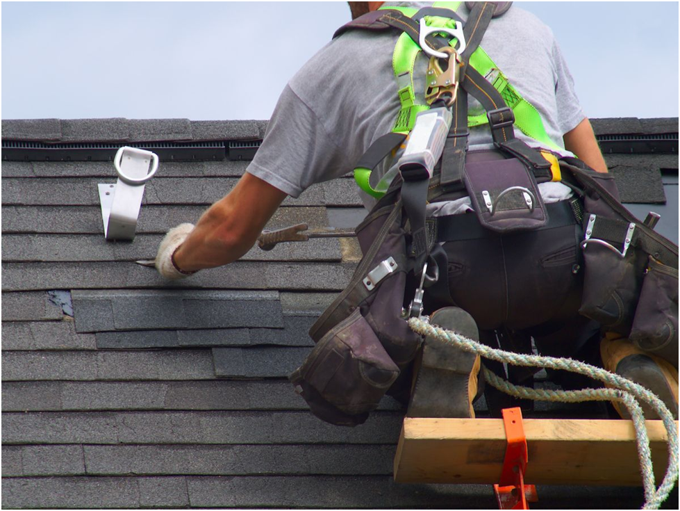 Roofer in safety harness repairing asphalt shingles