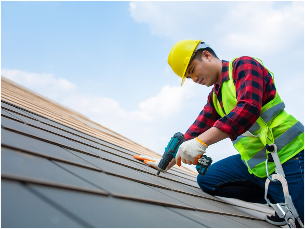 Roofer installing metal panels with drill on sloped roof