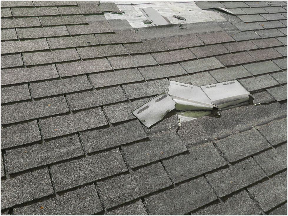 Damaged asphalt shingles on roof with missing patch
