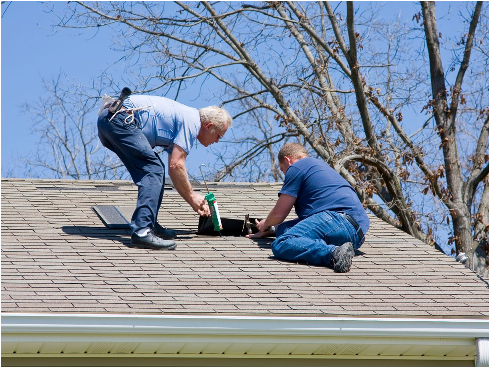 Two roofers repairing asphalt shingles on sloped roof
