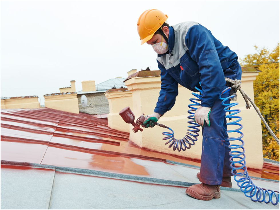Roofer spray painting red coating on metal roof