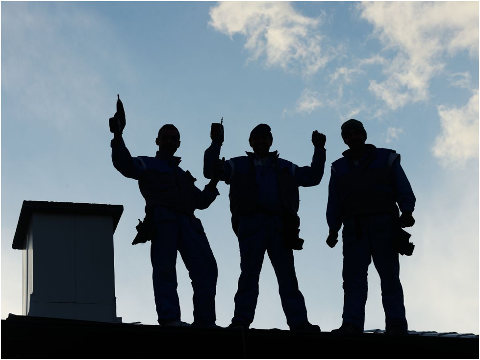 Silhouettes of roofers standing on a rooftop at sunset
