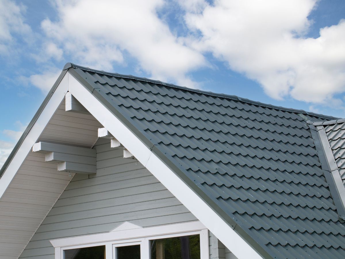 Gray metal tile roof on light gray house under blue sky